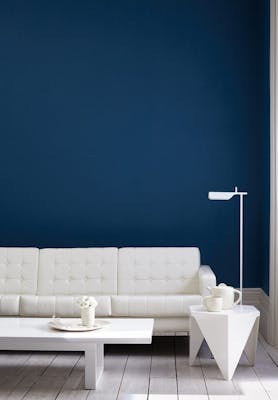 Living room painted in dark blue (Royal Navy) with a white sofa, lamp, table and wooden floor.