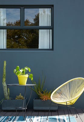 Outside dining area with a dark blue wall (Hicks' Blue) and bright yellow chair with a small table and plants.