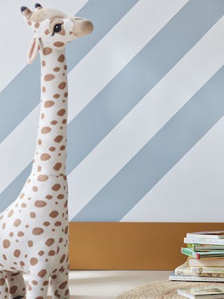 Child's reading corner painted in white (Shirting) with pale blue (Bone China Blue) diagonal stripes with a book shelf on the wall and a stuffed giraffe, table and chair.