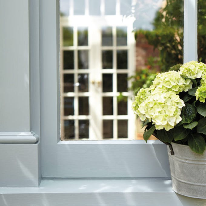 Light blue exterior window frame with a flower pot on the window sill and a white panelled door visible in the reflection.