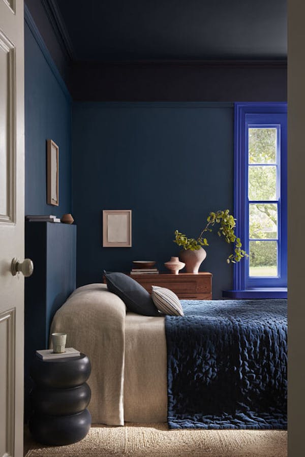 Bedroom painted in rich blue shade 'Royal Navy' with a bright blue 'Smalt' window frame, dark blue on the ceiling and a bed under the window.