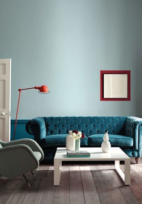 Large living room with pale blue walls and rich teal paint beneath the dado rail, with a large teal velvet sofa.