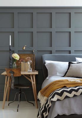 Paneled bedroom painted in dark grey 'Scree' with a small wooden desk next to a grey bed on a white floor.