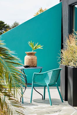 Outside dining area with blue green 'Canton' asymmetrical wall with dining room table and chairs with plants.