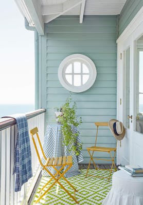 Sea front balcony painted in Celestial Blue with yellow (Bassoon) chairs, a round window and a green patterned floor.