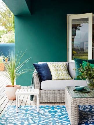 Outdoor dining area with dark green wall (Mid Azure Green) and wicker soda with table and a contrasting blue patterned rug.