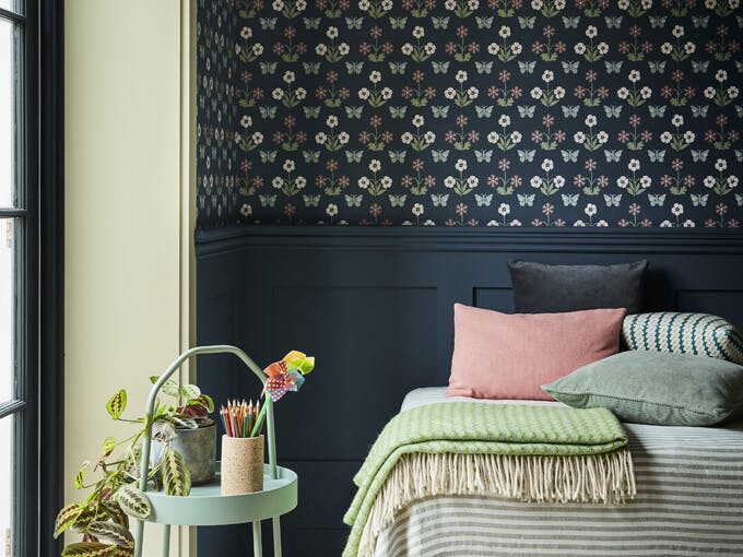 Bedroom featuring dark blue small print wallpaper (Burges Butterfly - Hicks' Blue) with a bed next to a large window and sidetable.