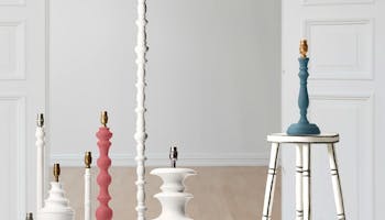 Seven wooden lamp bases from the Little Greene x Pooky collection displayed in a room with white and neutral colored walls.