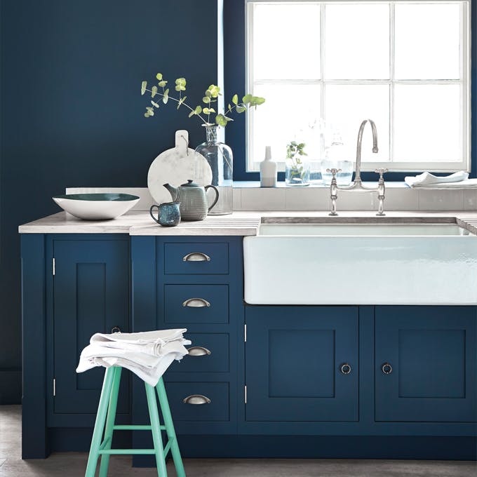 Kitchen painted in dark blue (Hicks' Blue) with a contrasting bright green (Green Verditer) stool underneath a window.