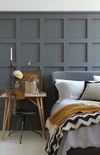 Paneled bedroom painted in dark grey 'Scree' with a small wooden desk next to a grey bed on a white floor.