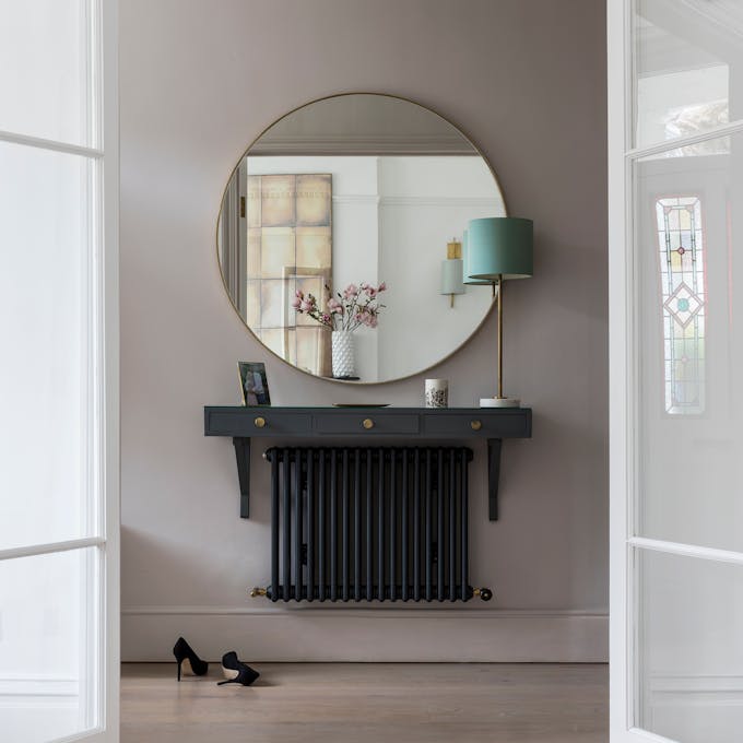 Interior double doors that open into a hallway with grey walls and a round mirror mounted above a side table and radiator.