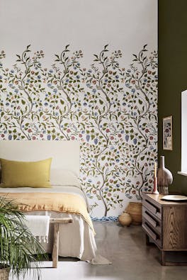 Bedroom with off white floral mural wallpaper (Mandalay - Ceviche) with a bed, sideboard and plant. 