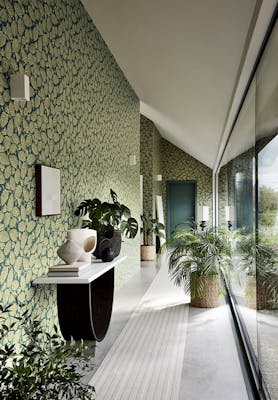 Long hallway with two tone blue and green wallpaper (Beech Nut - Florence) with a big window and plants.