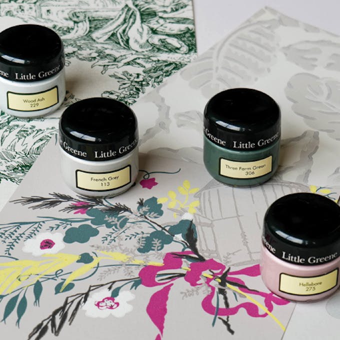 Three Little Greene wallpaper samples, a toile de jouy, a leaf print and a bold flower and bird pattern, four sample pots are placed ontop of the samples in the colours Wood Ash, French Grey, Three Farm Green and Hellebore 