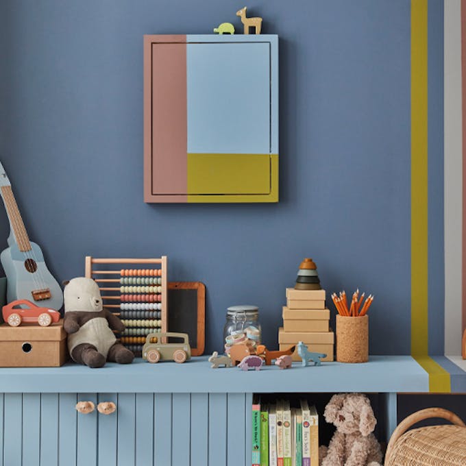 Child's playroom painted in dark blue (Juniper Ash) with multi colored stripes on the right, and toys placed on top of a unit.