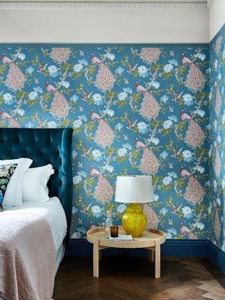 Bedroom with a blue bird print wallpaper (Pavona - Silvie) and a small wooden table next to the bed.