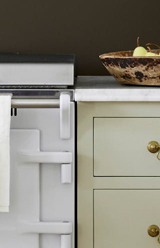 Close-up of a kitchen with black wall, silver appliances, white counter tops and light green drawers.