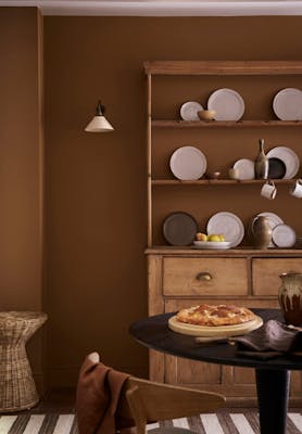 Dining space painted in orange-brown shade 'Galette' with a wooden dining table and a large wooden dresser and plates.