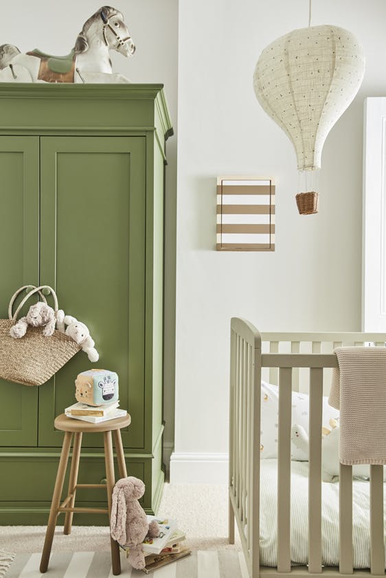 Calm nursery space with a green (Green Stone - Pale) wardrobe on the left and a crib on the right with a side table and fluffy toys on the floor.