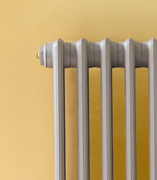 Close-up of a warm yellow wall painted in 'Yellow Gold' and mid-grey radiator in 'Urbane Grey'.