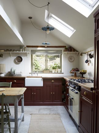 Cottage-style kitchen with dark brown-red cabinets and wooden worktops, alongside contrasting white walls and ceiling.