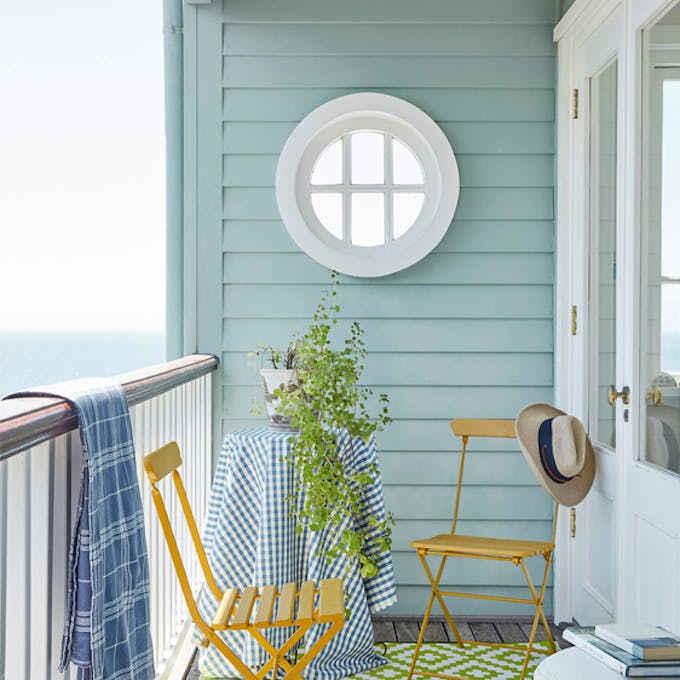 Sea front balcony painted in Celestial Blue with yellow (Bassoon) chairs, round window and a green patterned floor.