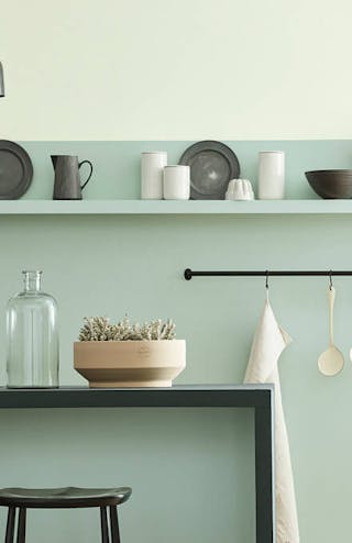 Kitchen space in varying shades of aquamarine with a breakfast bar and stools on a wooden floor.