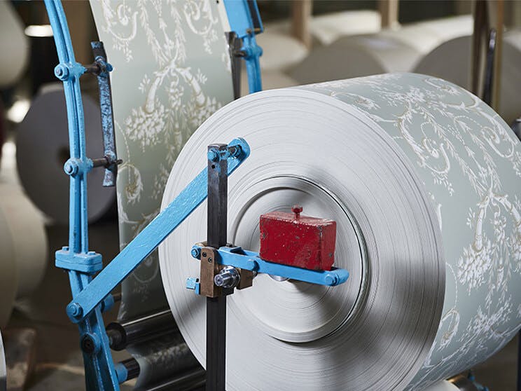 Panels of Little Greene grey patterned wallpaper rolled on a factory machine.