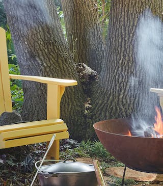 Forest with two bright yellow garden chairs (Giallo) with a barbeque lit surrounded by trees.