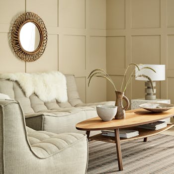 Paneled living space painted in warm neutral 'Travertine' with two sofas and a wooden coffee table.