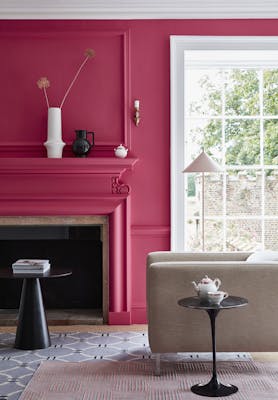 Living space painted in bright pink 'Leather' with a matching fireplace and  contrasting white window frame and an armchair.