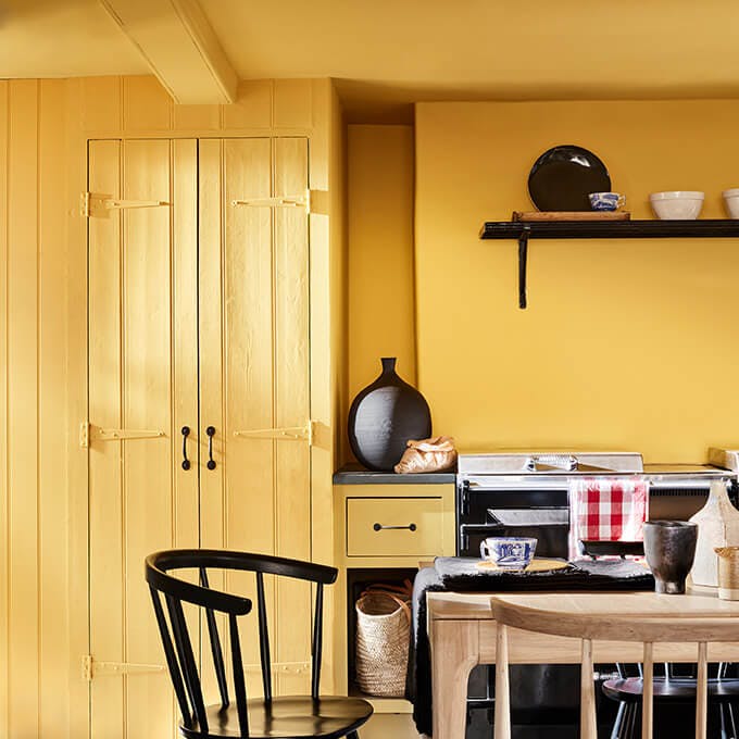 Kitchen color drenched in vibrant yellow shade 'Giallo', with a wooden table and chairs.