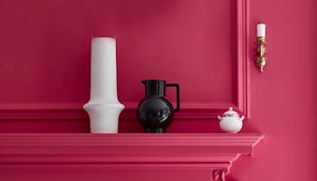 Wall and fireplace surround painted in bright pink 'Leather', alongside two contrasting vases in white and black.