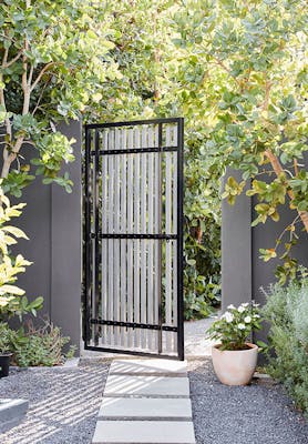 Garden gate with stepping stones and walls painted in grey shade 'Arquerite' with trees surrounding.