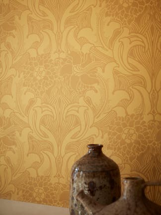 Close-up of Dahlia Scroll - Giallo yellow wallpaper on a wall with brown vases in the foreground.