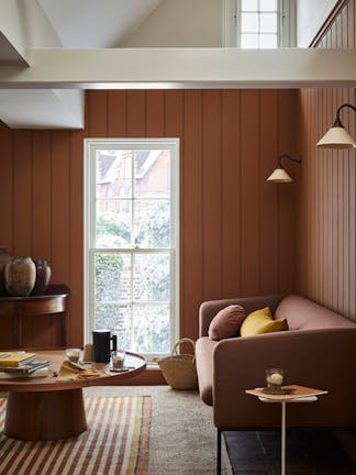 Paneled living area painted in caramel shade 'Affogato' with a matching sofa and striped rug next to a tall window.