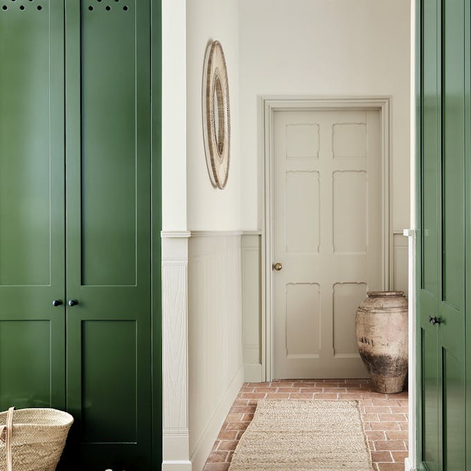 Hallway with dark green cupboard doors, neutral two-tone neutral walls and red brick flooring with a jute rug.