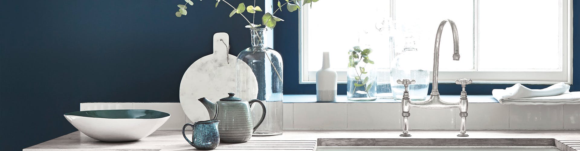 Close up of a kitchen painted in dark blue (Hicks' Blue) with white countertop and sink, in front of a large window.