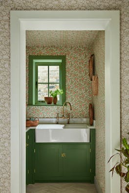 Pantry featuring two colourways of the floral wallpaper 'Spring Flowers' with dark green woodwork and a window above a sink.