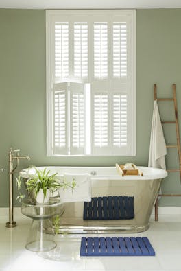 Bathroom painted in grey/ green 'Boringdon Green' with a silver bathtub under a large window.