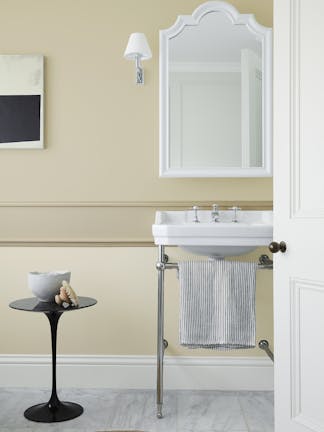 Bathroom painted in a different shades of warm neutral 'Travertine' with a free standing sink, white mirror and small table.