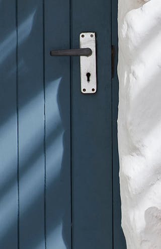 Close-up of an exterior deep blue (Hicks' Blue) and a white wall, with a seating area and striped cushions.