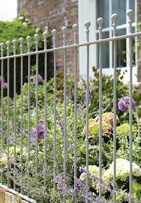 Metal railings outside of a house painted in mid gray shade 'Lead Color' with flowers and plants behind.