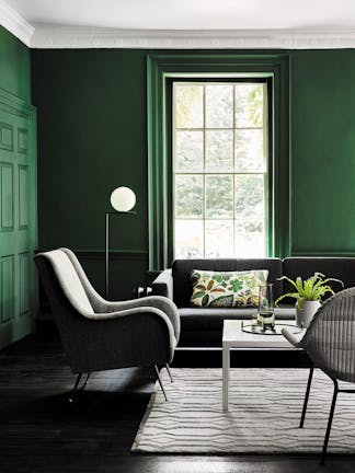 Living space painted in dark green (Puck) with a grey sofa, armchair and a white table on a rug.