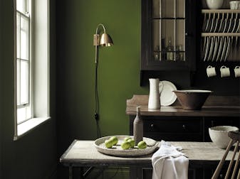 Dining area in deep green shade 'Jewel Beetle' with a wooden table and a rich brown 'Chocolate Color' dresser.