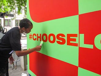 Woman adding final touches to the Choose Love mural with bright green paint in the nearly finished green and red section.