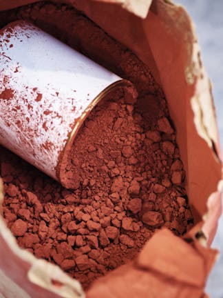 Close-up of a brown paper bag containing brown powder, with a white paint tin resting inside.