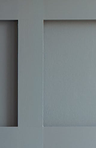 Close-up of a dark grey paneled wall painted in 'Scree', behind a bed with a grey headboard.