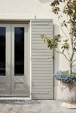 Back door with stone grey (Serpentine) shutters and off white (Slaked Lime -Deep) walls with a big potted plant on the right.