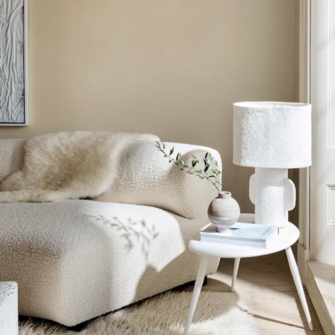 Living room in 3 different neutral shades (Silent White) with a sofa, table and lamp next to a window.